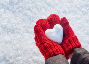 Person with read gloves holding a heart made of snow.