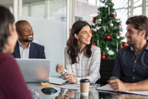Group of happy business people in meeting during Christmas holiday. Smiling businessman and businesswoman discussing new project strategy during x-mas time. Successful multiethnic business partners in a conversation in modern office.