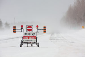 An emergency road closed barrier on the highway during a blizzard.